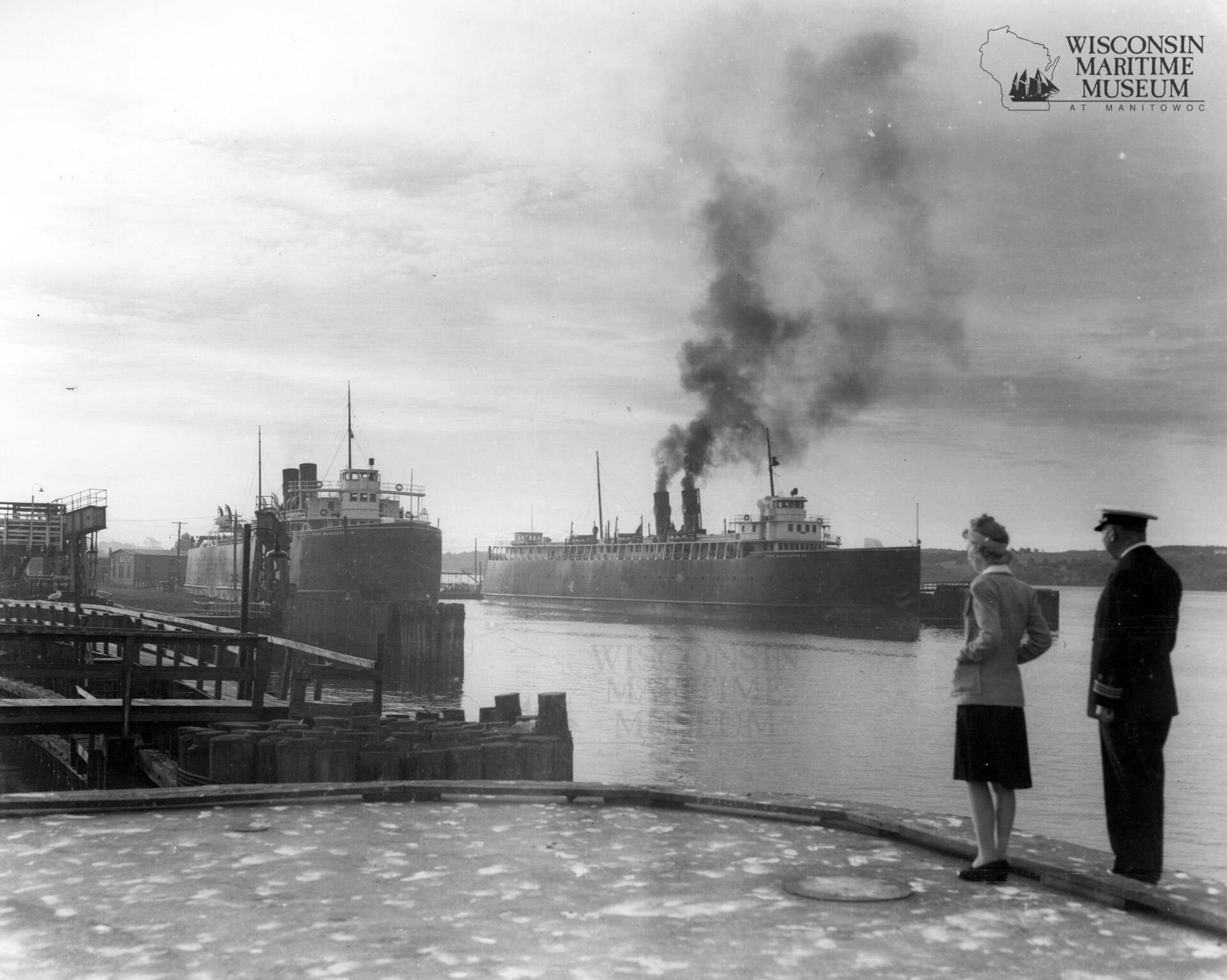 Black & white photo of a couple looking at a ship in the river.