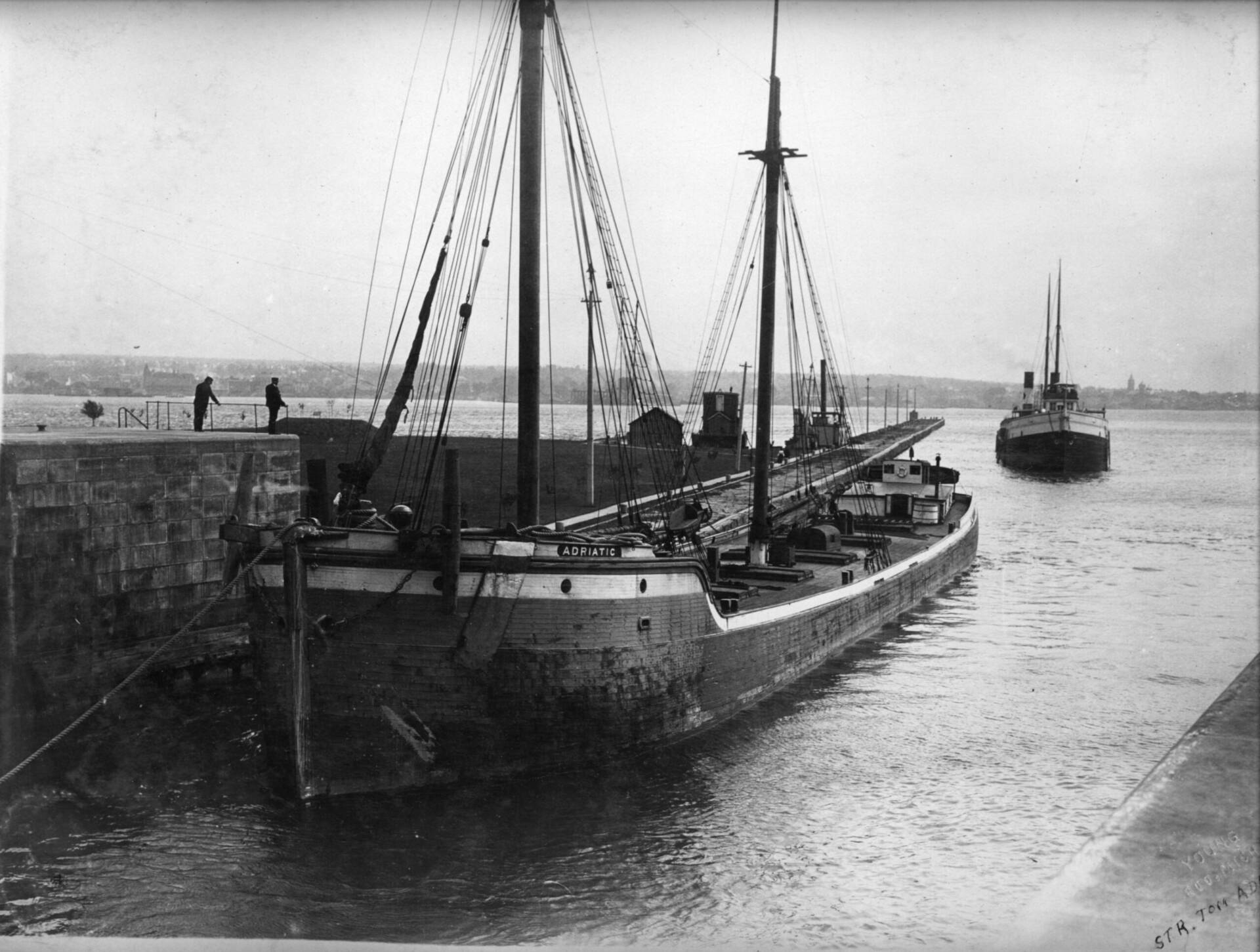 P82-37-007-89 A black and white photo of a long ship called ADRIATIC. The ship has two masts and an old self unloading bucket arm.